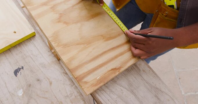 Placing plywood, man kneeling at workbench measuring with tape and pencil for cutting, copy space