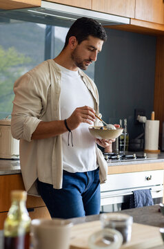 Man in his 30s holding ceramic bowl and stirring with spoon at home kitchen counter