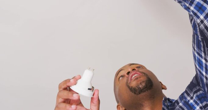 African American man checking plug and installing white recessed light into home ceiling