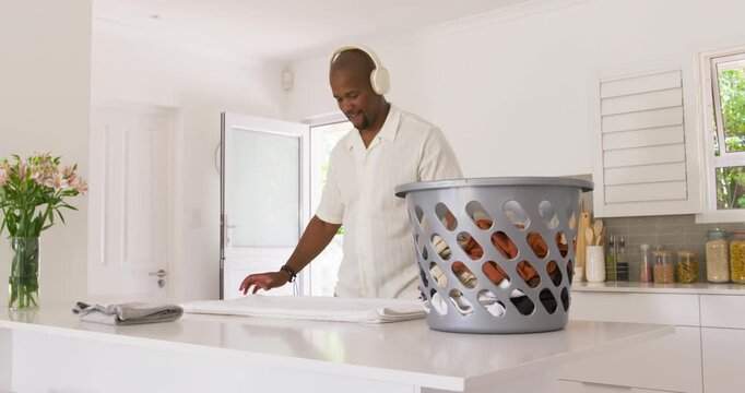 African American man lifting and folding towels from laundry basket at kitchen island making stack