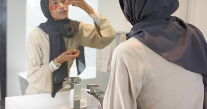 African American woman with scarf picking orange gel patches from jar, treating under eyes at sink