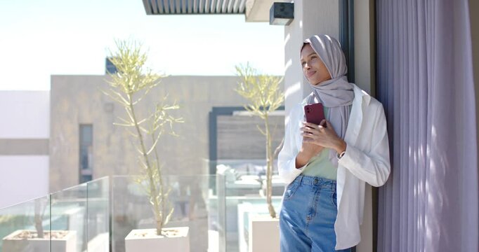 African American woman leaning on balcony door holding red phone gazing outward, copy space