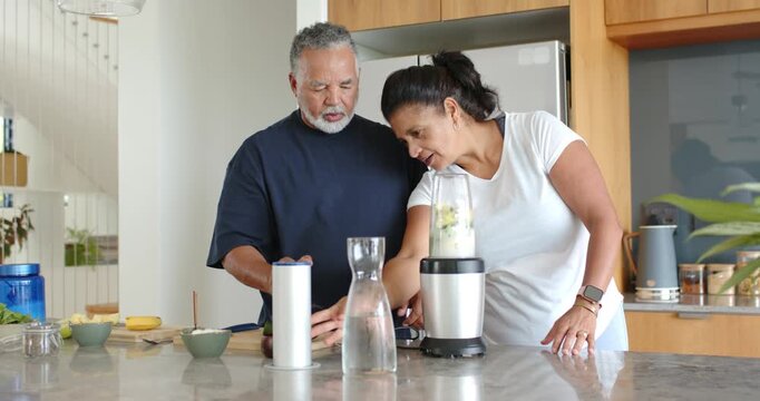 African American couple using phone, man tapping, woman holding blender on kitchen island for drink