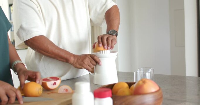 African American couple placing halves on juicer, man pressing, woman slicing for juice in kitchen