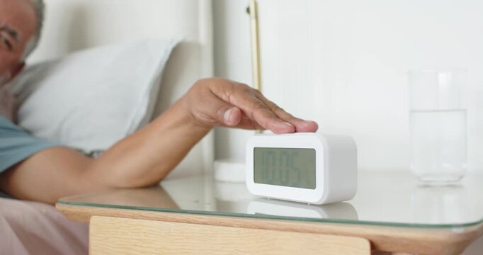 Senior African American man tapping digital alarm clock bedside silencing ringing alarm, copy space