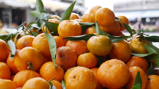 Fresh mandarins with green leaves piled together for sale at a fruit market stall, creating a bright orange display of citrus fruits commonly seen at local street markets. Fruit market.