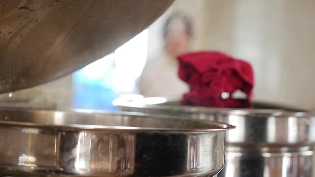 A female hand raises the lid of a hot food container on a self service counter with steam rising above prepared dishes inside a dining hall interior. Hospitality service.