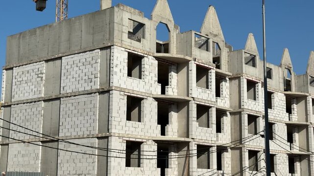 Unfinished apartment building with aerated concrete blocks under blue sky, exposed balconies and repetitive window openings, crane.