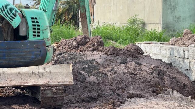 An excavator levels soil beside a concrete structure while preparing terrain for further engineering activity on a structured construction site surface. Engineering work.