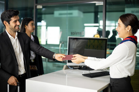 Smiling business traveler handing passport to airline staff at airport check-in counter for identity verification and document processing