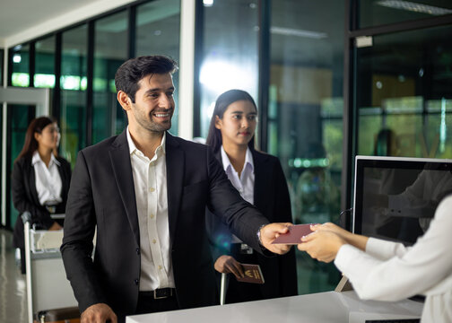 Business travelers at airport check-in counter handing passport to airline staff for identity verification and document processing