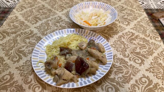 Plate pork slices fried porcini mushrooms with creamy noodles and tangy cabbage coleslaw on patterned linen in cozy restaurant