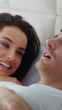 Happy Caucasian couple man woman lying on bed home bedroom cozy talking smiling conversation discussion chatting female male husband wife bonding love relaxing togetherness speak girlfriend boyfriend