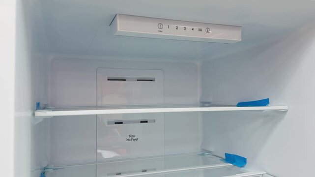 Empty refrigerator interior with glass shelves, pristine white cavity, overhead LED illumination, adjustable glass racks with blue