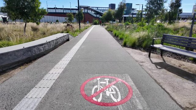 Shared pedestrian pathway outside Deer Park railway station in Melbourne, Australia, featuring a cyclist dismount marking and tactile paving. Public transport precinct, pedestrian priority