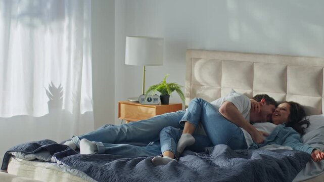 Happy Caucasian couple man jumping on bed hugging woman at home bedroom laughing family husband wife girl guy together hugging smiling fun cuddle honeymoon love feelings sweetheart female male romance