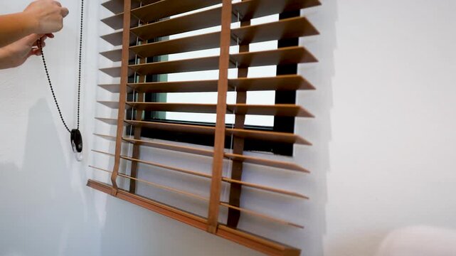 Hands Adjusting Wooden Venetian Blinds to Control Sunlight in Home Office