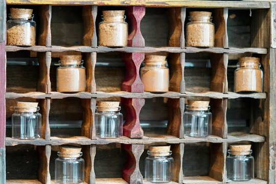 Vintage wooden bottle crate turned into a spice rack. Small glass bottles of cinnamon along with empty bottles with cork lids.
