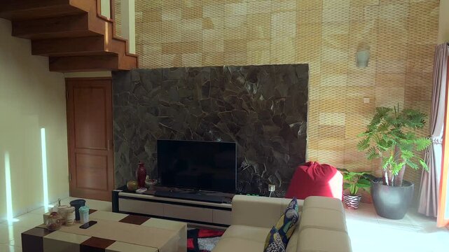 Modern living room with stone wall, flat tv and bright furniture decoration. Wooden stair