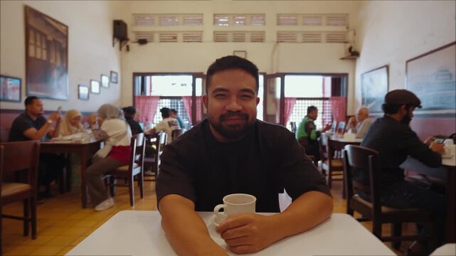 A man drinking coffee while talking to the camera in a cafe, creating a point of view conversation as if on a casual meeting date. Warm friendly atmosphere with direct eye contact social interaction.