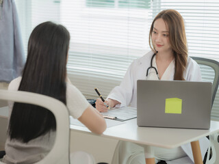 An Asian female doctor is talking to a patient, conversing while seated at a table about concepts of medicine and healthcare.