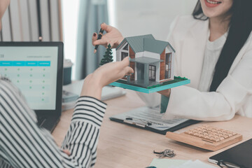 Two female real estate agents are working in an office; one is showing a model home and using a calculator to explain mortgages and interest rates to a client.