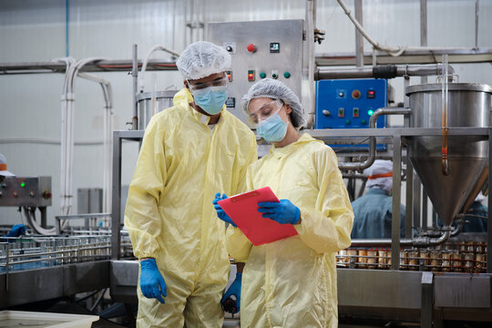 Two industrial engineer supervisors inspect and examine quality control, production process at automate conveyor in canned food manufacturing factory, and protective uniforms for hygiene operations.