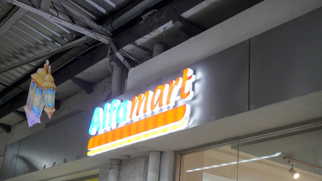 Purwokerto, Indonesia - 23 March 2026: Alfamart convenience store illuminated signage at shopping mall entrance, glowing blue and yellow logo.