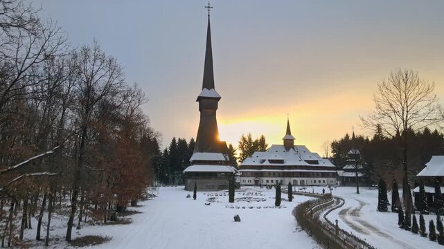 Winter aerial view of sapanta peri wooden monastery in romania during golden sunset with snow ground.
