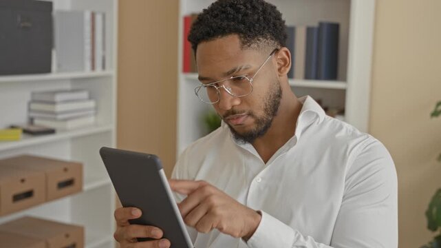 Man taps tablet screen with finger in office building with glasses and white shirt; concentration productivity.