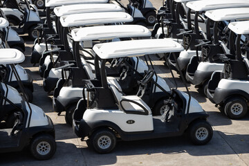 Rows of identical golf carts lined up on sunny gravel lot © Rattanachat