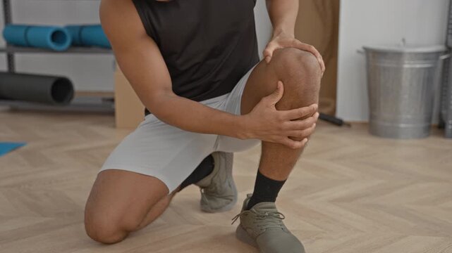 Man holding knee with both hands while kneeling in studio for fitness training; rehab recovery focus.