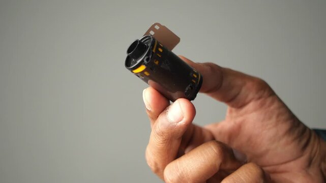Person holding vintage thirty five millimeter film canister against plain gray background.