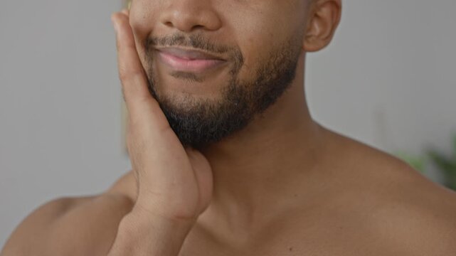 Man touching beard and chin with hand, shirtless in studio showing grooming gesture and gentle smile; confidence selfcare.