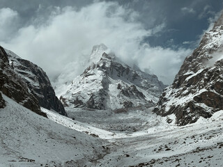 A massive snow-covered Himalayan mountain peak towering over a rugged glacial valley under a dark dramatic sky. © Rohan