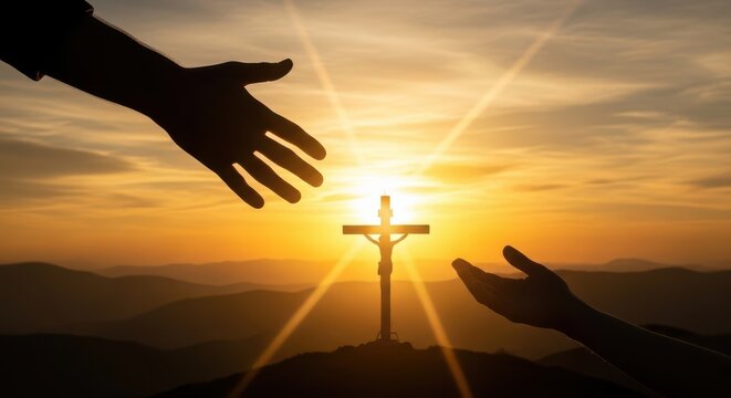 A silhouette of two hands reaching out towards a crucifix at sunset on a mountain