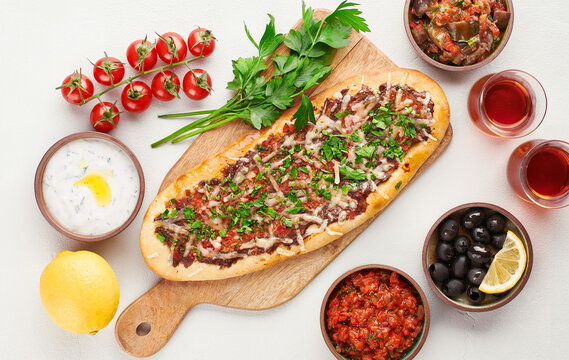 Turkish pide with minced meat, cheese and parsley with traditional meze, olives, yogurt sauce and tea, top view.