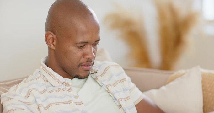 African American adult male sitting on couch in striped shirt and jeans, looking at laptop, typing