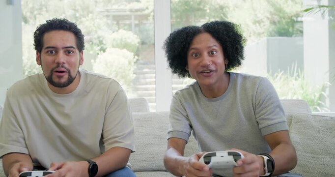 African American friends cheering after win on couch in living room, patting with white controllers