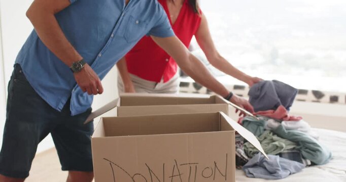 Couple finding donation box, sorting clothes on bed, holding pink or coral, blue or gray shirts, dec