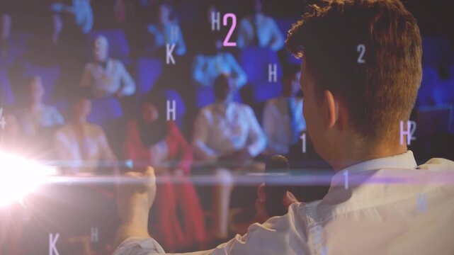 Presenter gesturing and speaking onstage activating floating alphanumeric graphics showing data