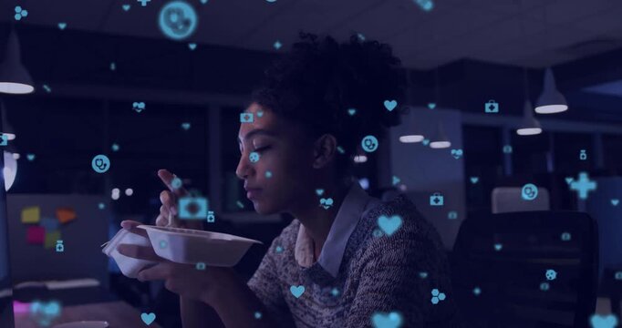 Vertical video: Woman eating at desk working late, watching screen, floating health icons over her