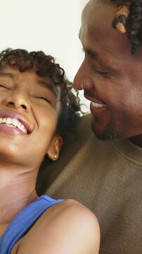 Vertical video: Leaning pair laughing and watching on sofa at home blue tank brown top showing love