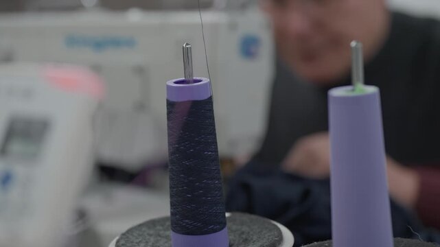 Two dark navy thread cones on sewing machine spindle pins with blurred worker in background