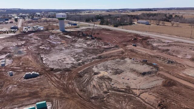 High angle aerial shot of a massive land clearing and construction project in Erin, Ontario, featuring heavy machinery and a local water tower. Ideal for urban development and industrial growth storie