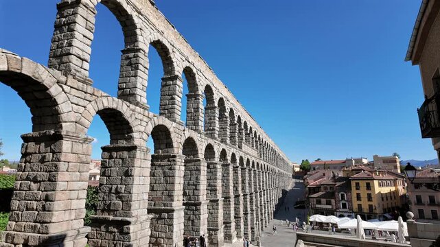 Cinematic reveal of Segovia aqueduct with repeating arches and strong depth under bright blue sky.