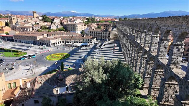 Elevated wide view of Segovia aqueduct and city square with long shadows under clear blue sky.