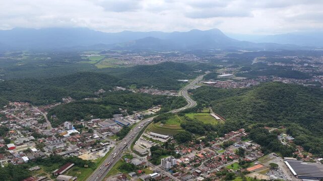 Aerial view of BR-101 highway cutting through Joinville with urban areas, forest and mountains in Brazil.