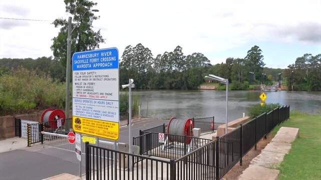 Road leading to Sackville vehicle ferry crossing with river, signage, and loading ramp ahead, Australia