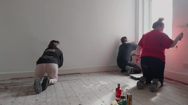 A team of three family members in Glasgow, Scotland, collaborating on a home renovation project. They are painting walls in a vacant property, preparing the interior for a successful real estate sale